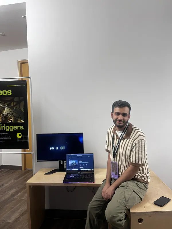 Dhruv standing next to the BlitzMind exhibition setup — poster on the left, demo monitor on the right